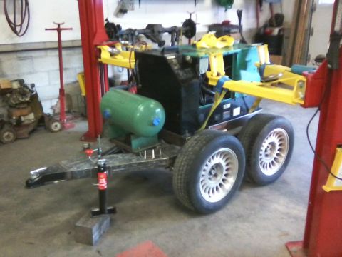 1984 Honda ATC 250 R - A trailer with a green tank and yellow arms is parked in a garage, with a jack supporting the hitch.