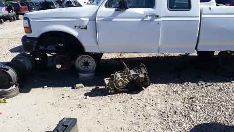 1985 Ford Bronco - Transmission removed from a white Ford F-Series truck in a junkyard.