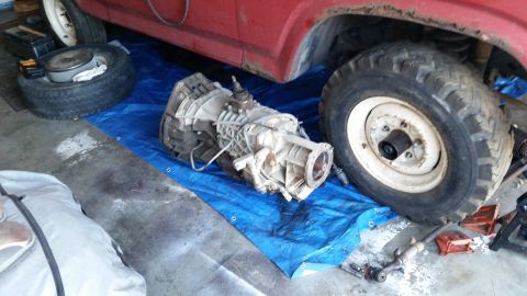 1985 Ford Bronco - A vehicle transmission is laid out on a blue tarp, with a red vehicle partially visible above.