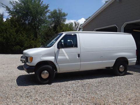 1999 Ford E250 - This 1999 Ford E250 cargo van is captured in a side profile, parked on a gravel surface.