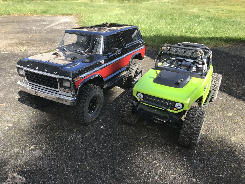 Black Bronco-style RC car with red stripe next to a lime green RC Jeep-like vehicle