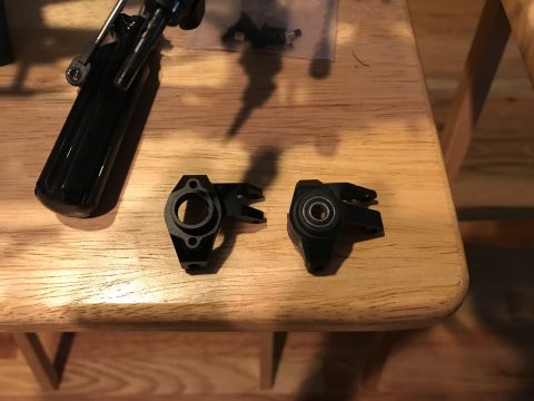 1989 Ford Bronco - RC car steering knuckles and a part of the suspension assembly are laid out on a wooden surface.