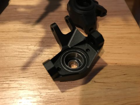 1989 Ford Bronco - Close-up of two black metal suspension knuckles, likely for an RC car, resting on a wooden table.