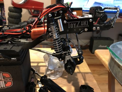 1989 Ford Bronco - Close-up of an RC car chassis, showing the suspension system, motor, and "TOY/UKI" branding.