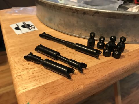 1989 Ford Bronco - Several black automotive suspension parts are laid out on a wooden table next to a metal container.