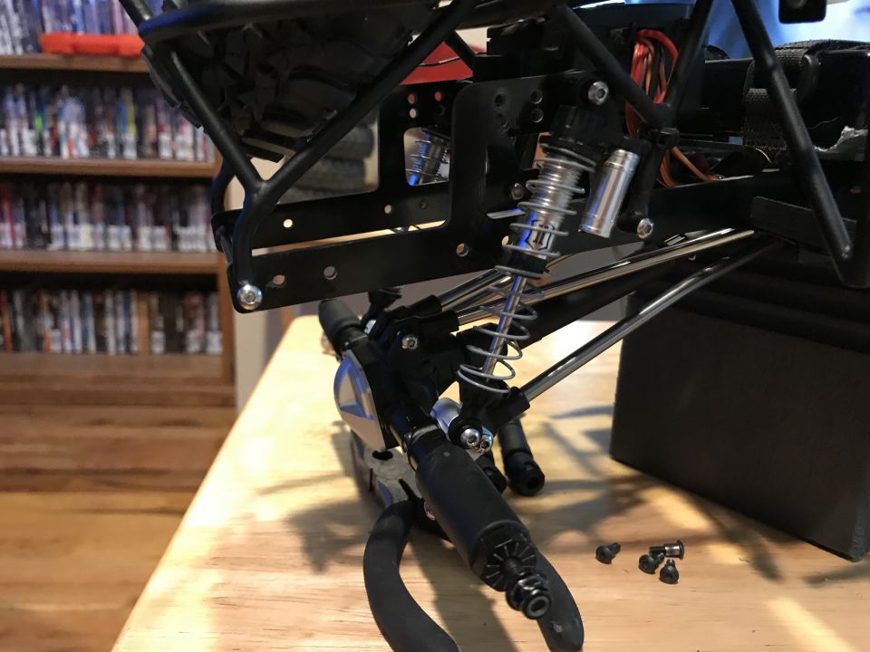 RC car chassis with shocks and suspension components, with pliers and screws on a wooden surface