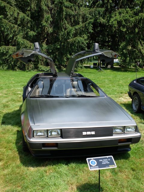 1971 Ford Ranchero - A DeLorean DMC-12 is displayed with its iconic gullwing doors open on a sunny day.