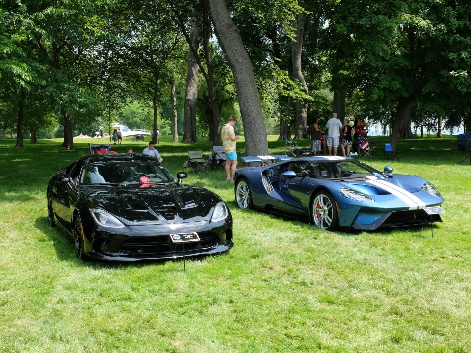 Black Dodge Viper and blue Ford GT parked on grass with trees in background