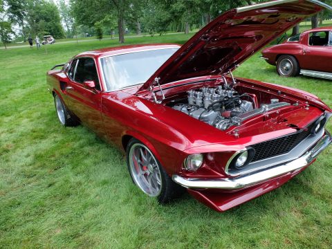 1971 Ford Ranchero - A custom 1969 Ford Mustang Mach 1 is displayed with its hood open, revealing a powerful engine, while another classic car sits nearby.
