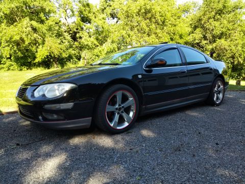 2002 Chrysler 300M - A black sedan is parked on a gravel surface with trees and grass visible in the background.