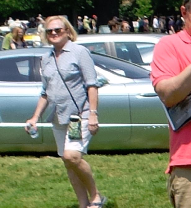 Woman in sunglasses and a striped shirt walks past a silver car at an outdoor event
