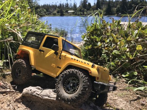 1989 Ford Bronco - A yellow remote control Jeep Wrangler Rubicon navigates a rocky trail beside a lake.