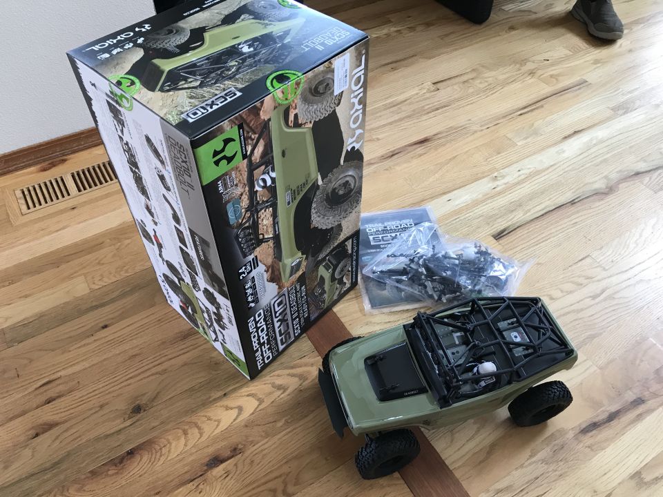 RC rock crawler vehicle next to its box, with extra parts and instructions on the floor