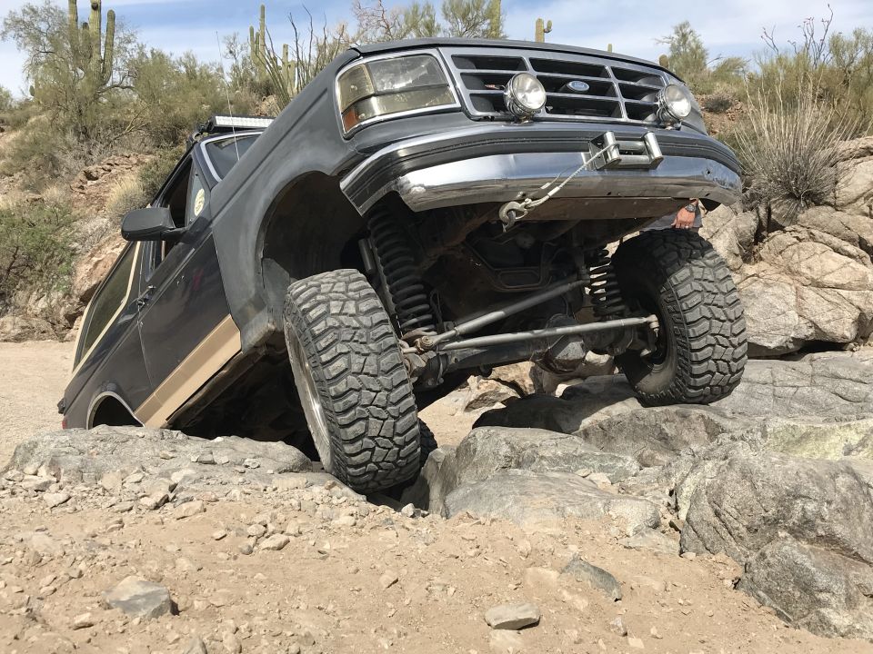 Ford Bronco navigating rocky terrain, front wheel high off the ground