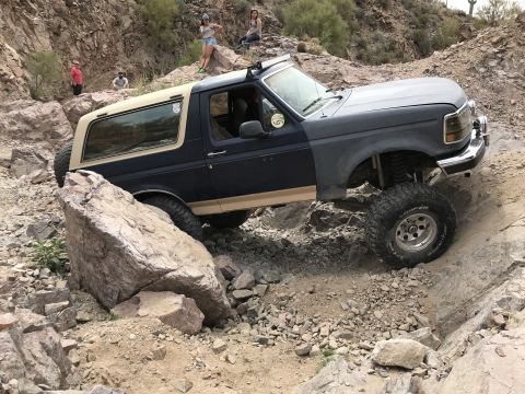 1991 Ford Bronco - A modified Ford Bronco navigates a rocky trail with people watching from the hillside.
