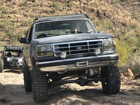 1991 Ford Bronco - Modified Ford Bronco and a UTV navigate a desert trail with cacti and rocky terrain.