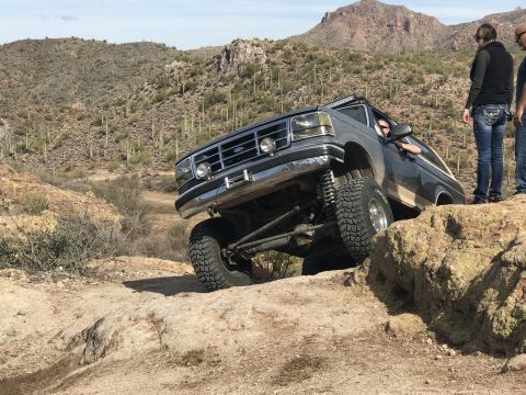 1991 Ford Bronco - A lifted Ford Bronco navigates a rocky desert terrain with a driver and onlookers present.