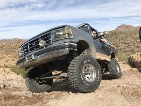 1991 Ford Bronco - This lifted Ford Bronco navigates a challenging desert terrain with its large off-road tires.