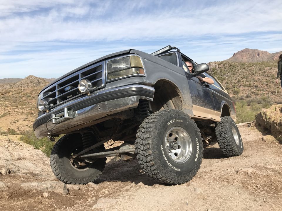 Gray Ford Bronco with lifted suspension and off-road tires driving on a rocky desert trail