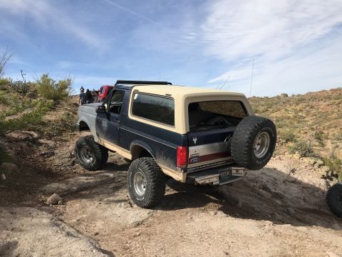 1991 Ford Bronco - This 1991 Ford Bronco is seen from the rear, navigating a rocky off-road trail with other vehicles in the background.