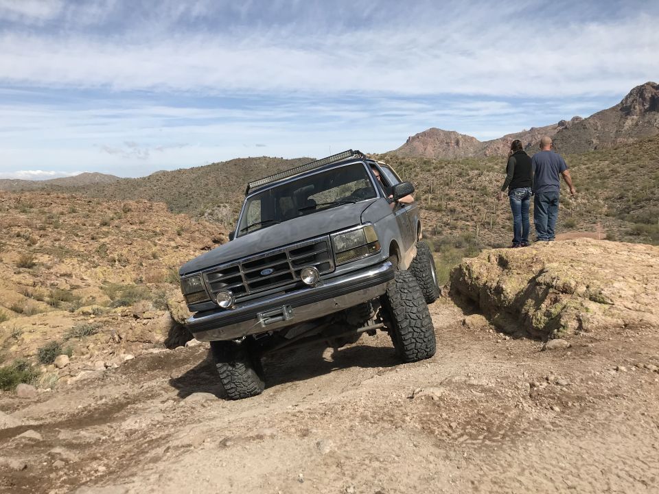 Gray Ford Bronco climbing rocky terrain with two people watching