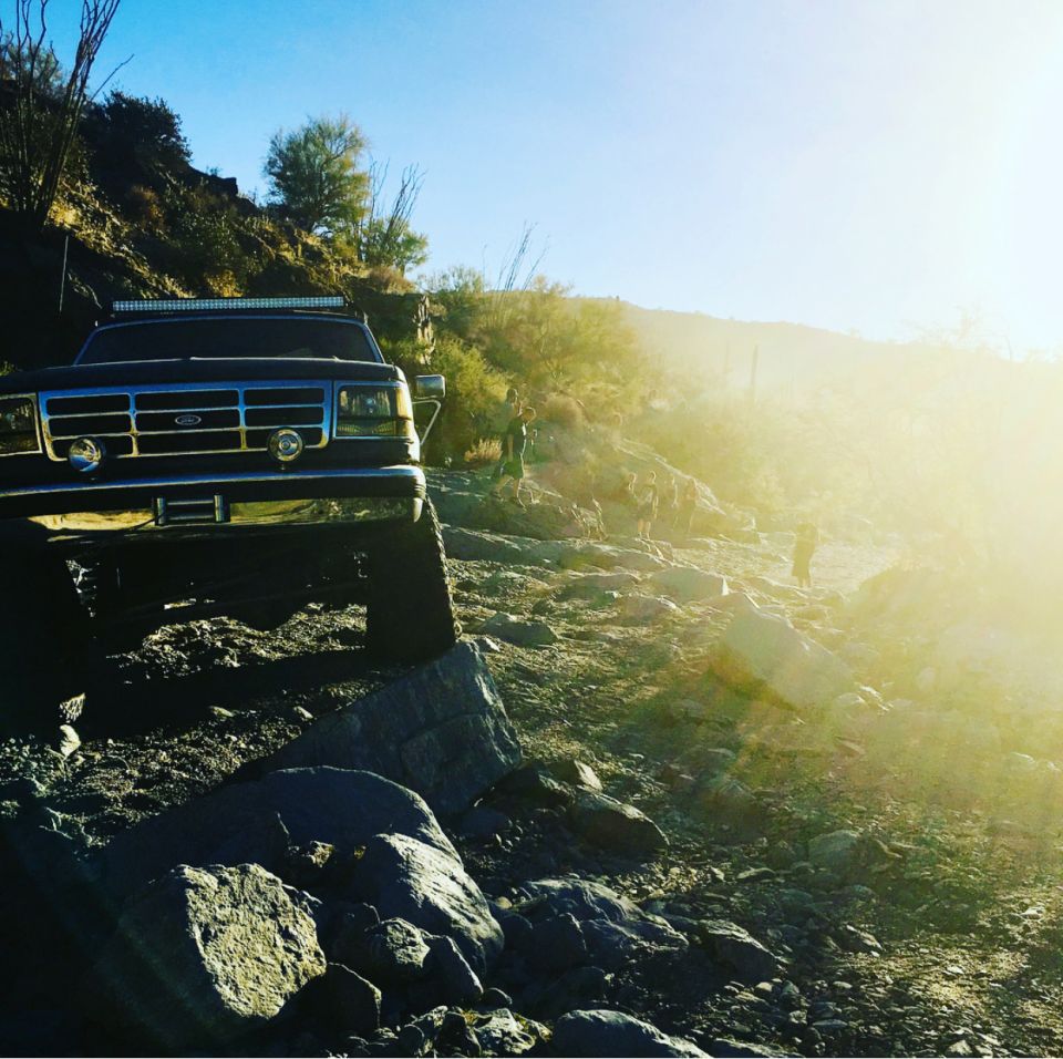 Dark blue Ford Bronco on rocky terrain, front 3/4 view, with light bar on roof