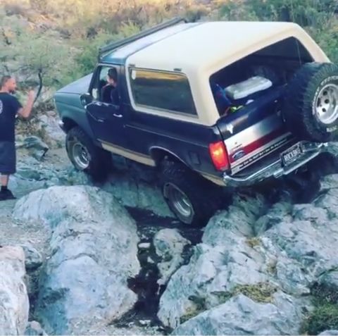 1991 Ford Bronco - A Ford Bronco is shown off-roading over large rocks, with a person standing nearby.