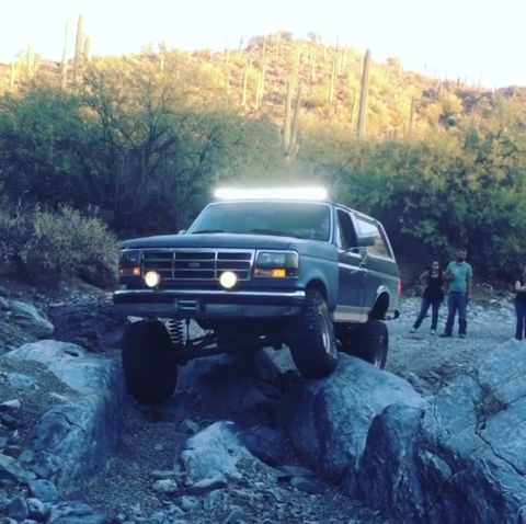 1991 Ford Bronco - A lifted 1991 Ford Bronco navigates a rocky desert trail with cacti in the background.