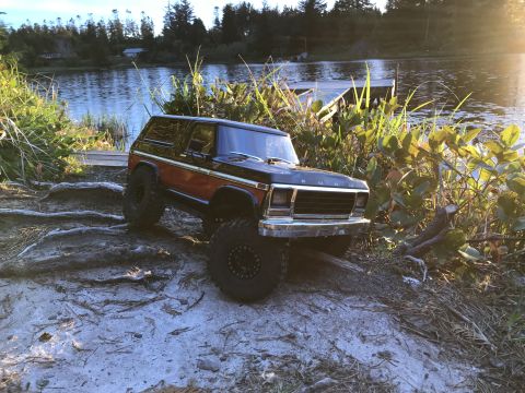 1989 Ford Bronco - Remote control Bronco sits on sandy shore near water and vegetation.