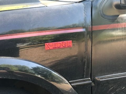 2000 Ford Explorer - Close-up of a red X-EDGE emblem on a black vehicle's fender.
