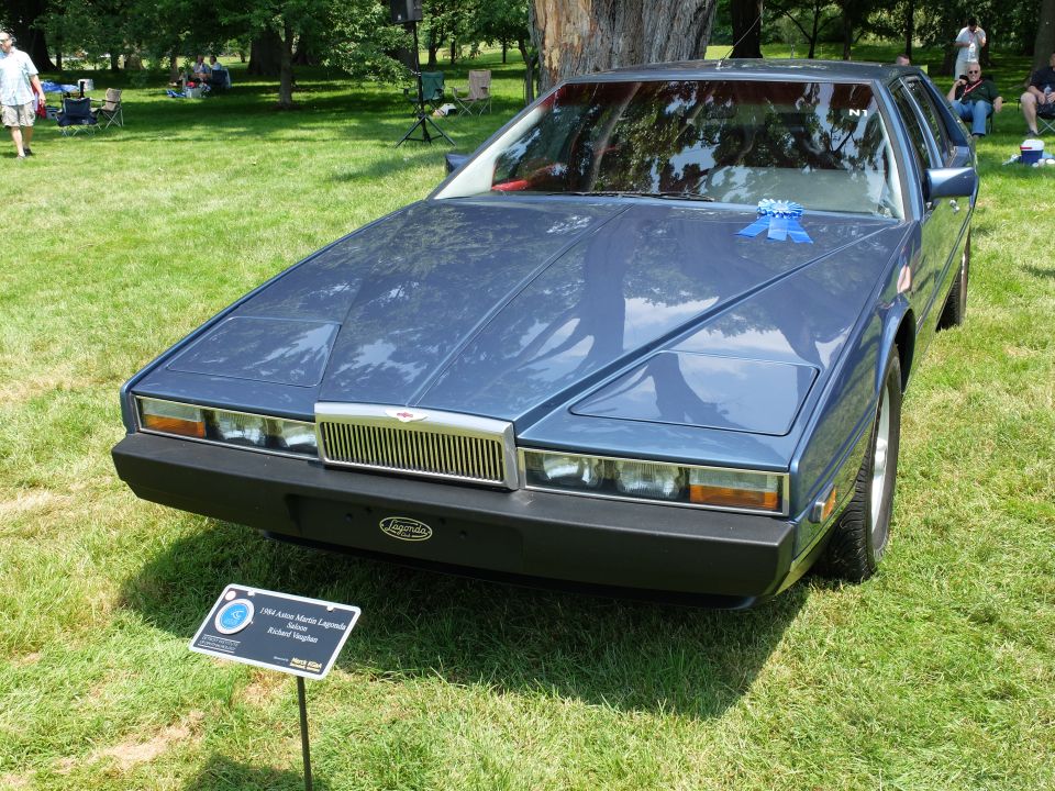 Blue Aston Martin Lagonda with a blue ribbon on the hood, parked on grass