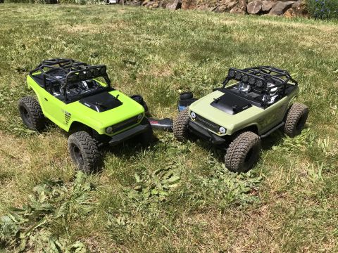 1989 Ford Bronco - Two remote control off-road vehicles are parked on a grassy area with rocks in the background.