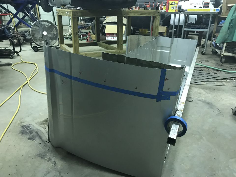 Gray truck bed panel with blue tape markings, seen from a low angle in a workshop