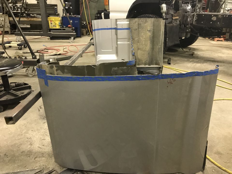 Unfinished truck cab section with blue tape on edges, in a workshop setting