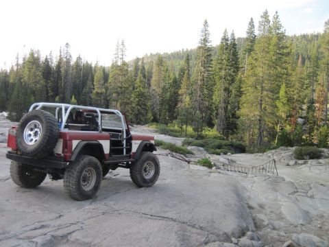 1968 Ford Bronco - Modified 1968 Ford Bronco parked on rocky terrain with a forest in the background.