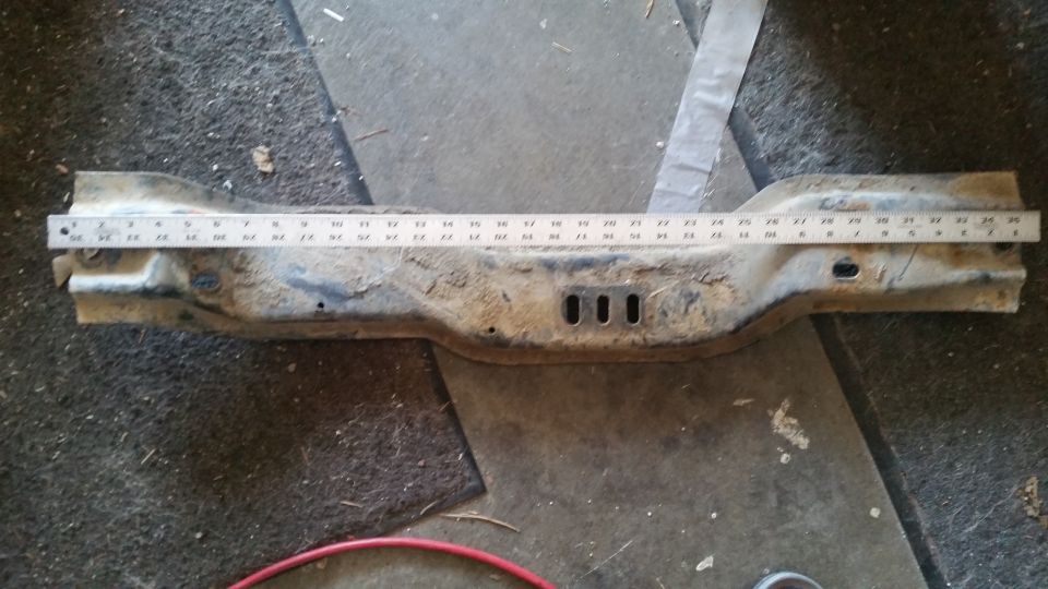 Rusted metal crossmember with a ruler laid across it for measurement