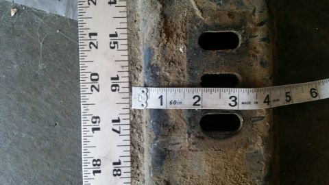 1985 Ford Bronco - A tape measure is used to measure the width of a metal component with several holes.