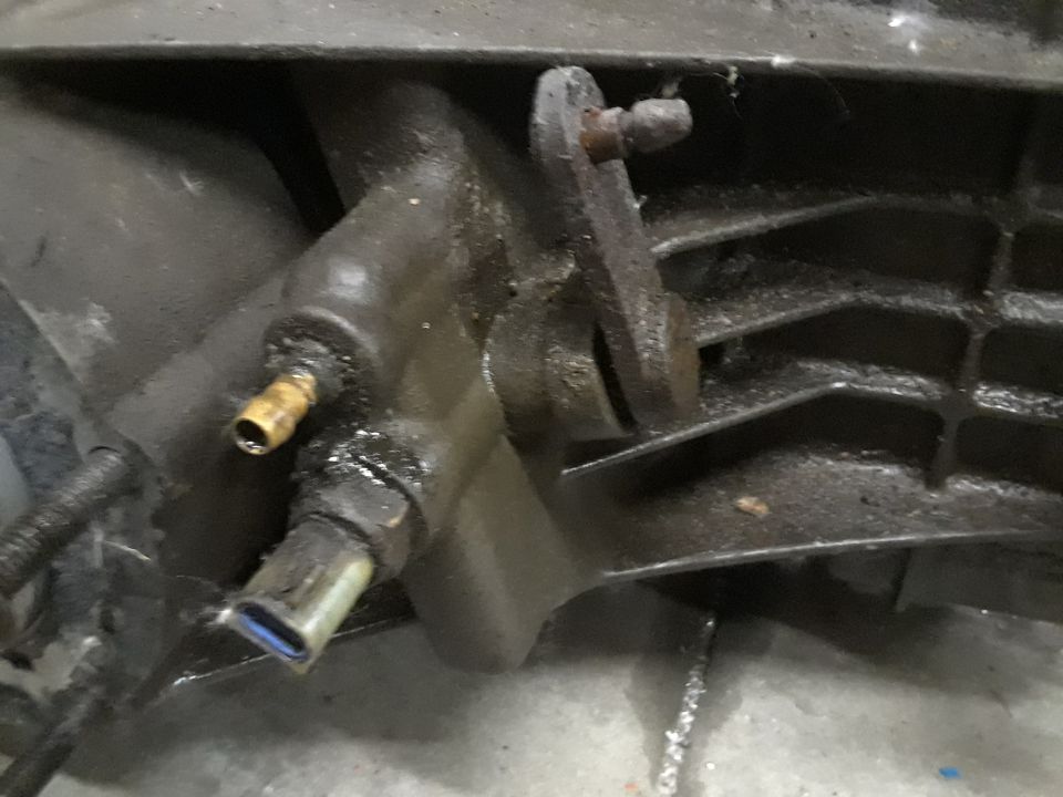 Close-up of a greasy transfer case with a metal lever and a brass fitting