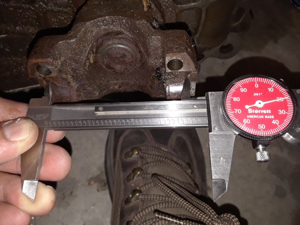 Rusty metal part being measured with a caliper and a red dial indicator