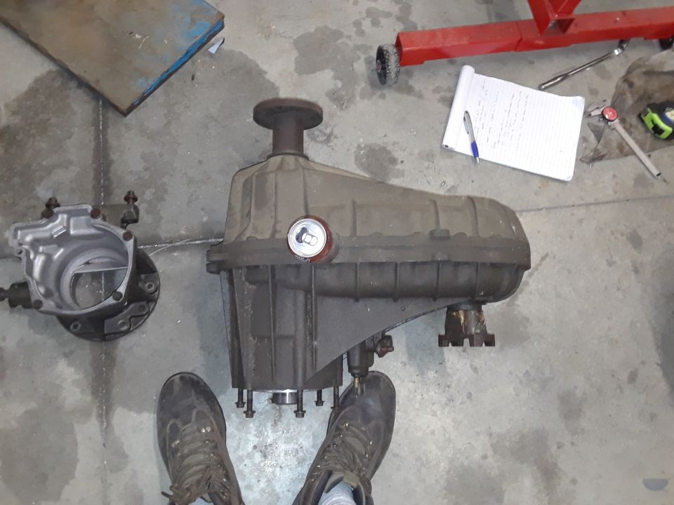 Transfer case on a garage floor next to its housing. A notebook and pen are nearby