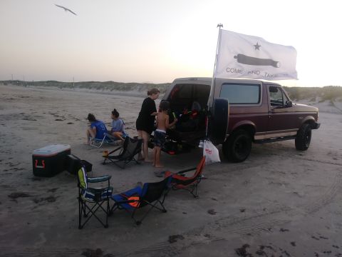 1996 Ford Bronco - People gathered around a truck on a sandy area with a flag in the background.