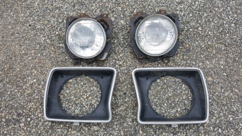 1978 Ford Bronco - A pair of vehicle headlights and their surrounding bezels are displayed on a gravelly surface.