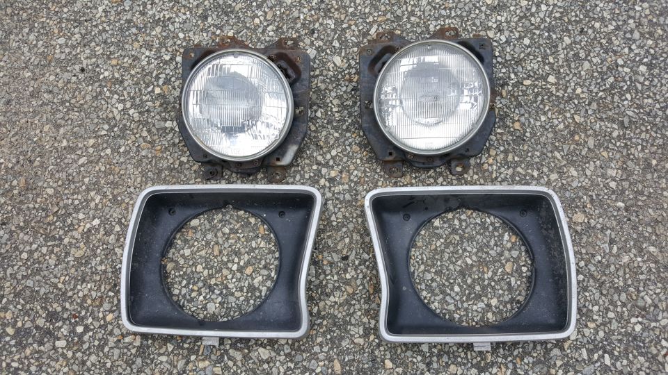 Two round headlights and two square bezels laid out on asphalt