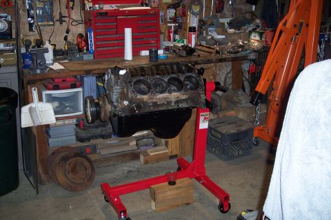 1995 Ford Bronco - Engine block on a red stand in a cluttered garage setting, surrounded by tools and equipment.