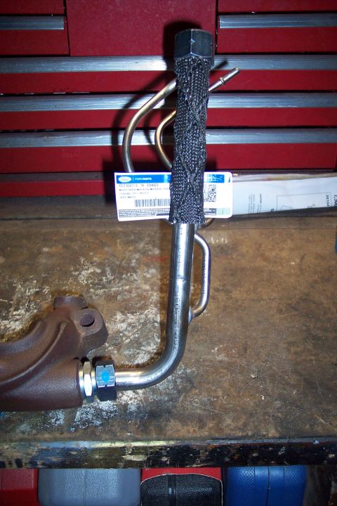 1995 Ford Bronco - Close-up of an exhaust manifold part with a braided heat shield and metal tubing, resting on a workbench.