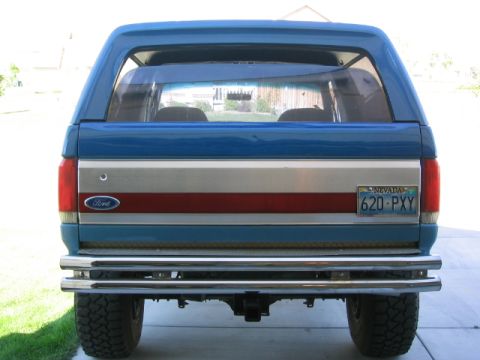 1989 Ford Bronco - Rear view of a blue 1989 Ford Bronco, a chrome bumper and a distinctive red and silver stripe on the tailgate.