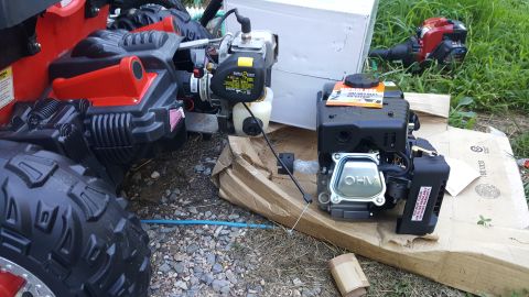 2007 Subaru Impreza - A new lawnmower engine sits on cardboard next to a red and black riding mower's chassis.