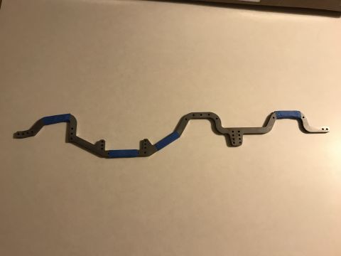 1989 Ford Bronco - A gray metal chassis component, possibly for an RC vehicle, is shown with blue tape applied to sections.