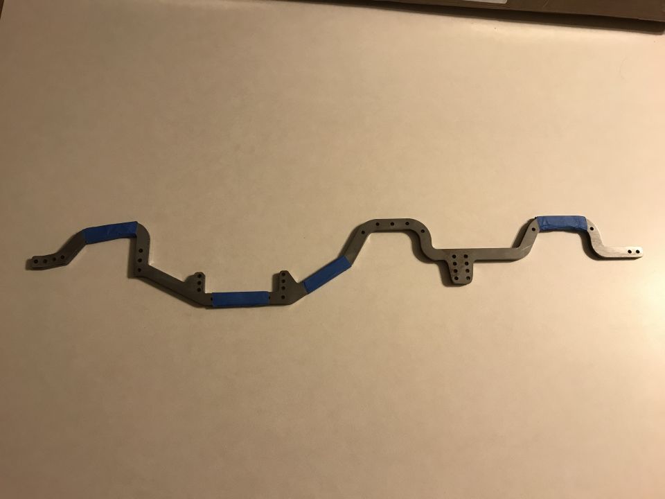 Gray metal chassis part with blue tape accents, viewed from above