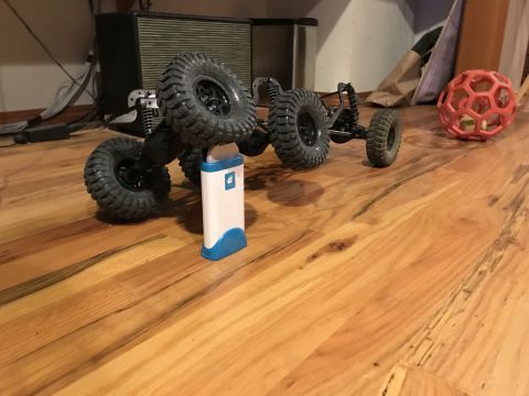 1989 Ford Bronco - A remote-controlled rock crawler toy is positioned on a wooden floor, with a small electronic device and a toy ball nearby.